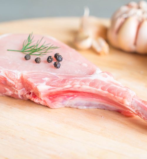 fresh pork chop on wood board with garlic and black peppers