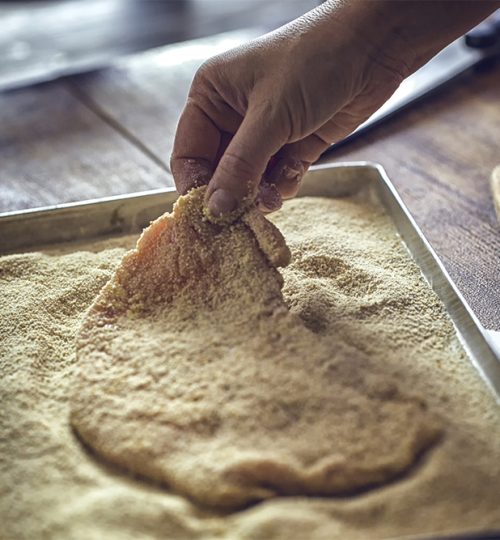 Preparing Wiener Schnitzel with beaten egg and bread crumbs